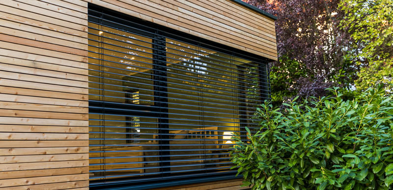 Fenster mit anthrazitfarbenem Raffstore an einer Holzfassade